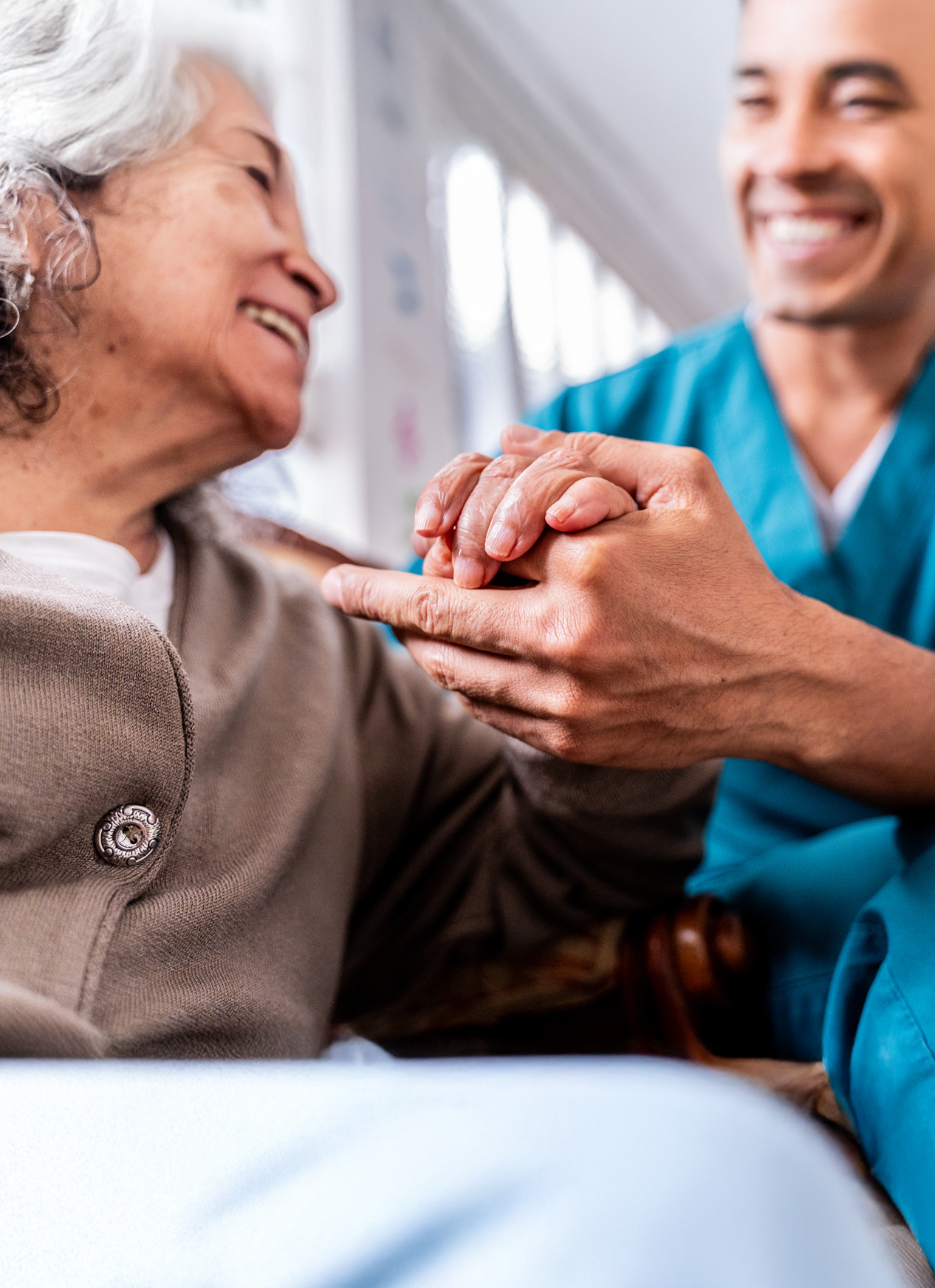 Cuidador sanitari somrient sostenint les mans d'una dona gran, tots dos compartint un moment de proximitat i suport.