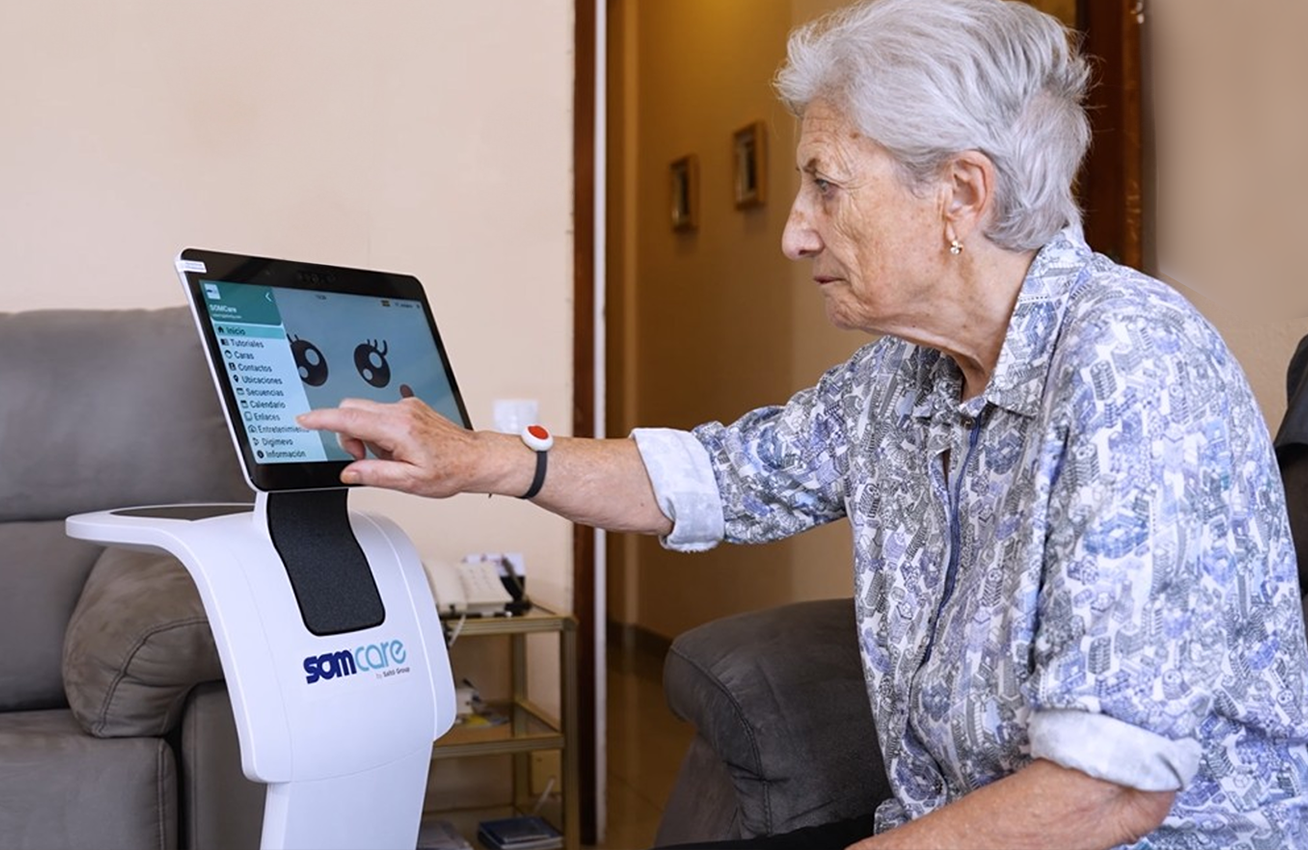 Mujer mayor interactuando con un robot asistencial en casa, tocando la pantalla táctil con menú de opciones y avatar animado.